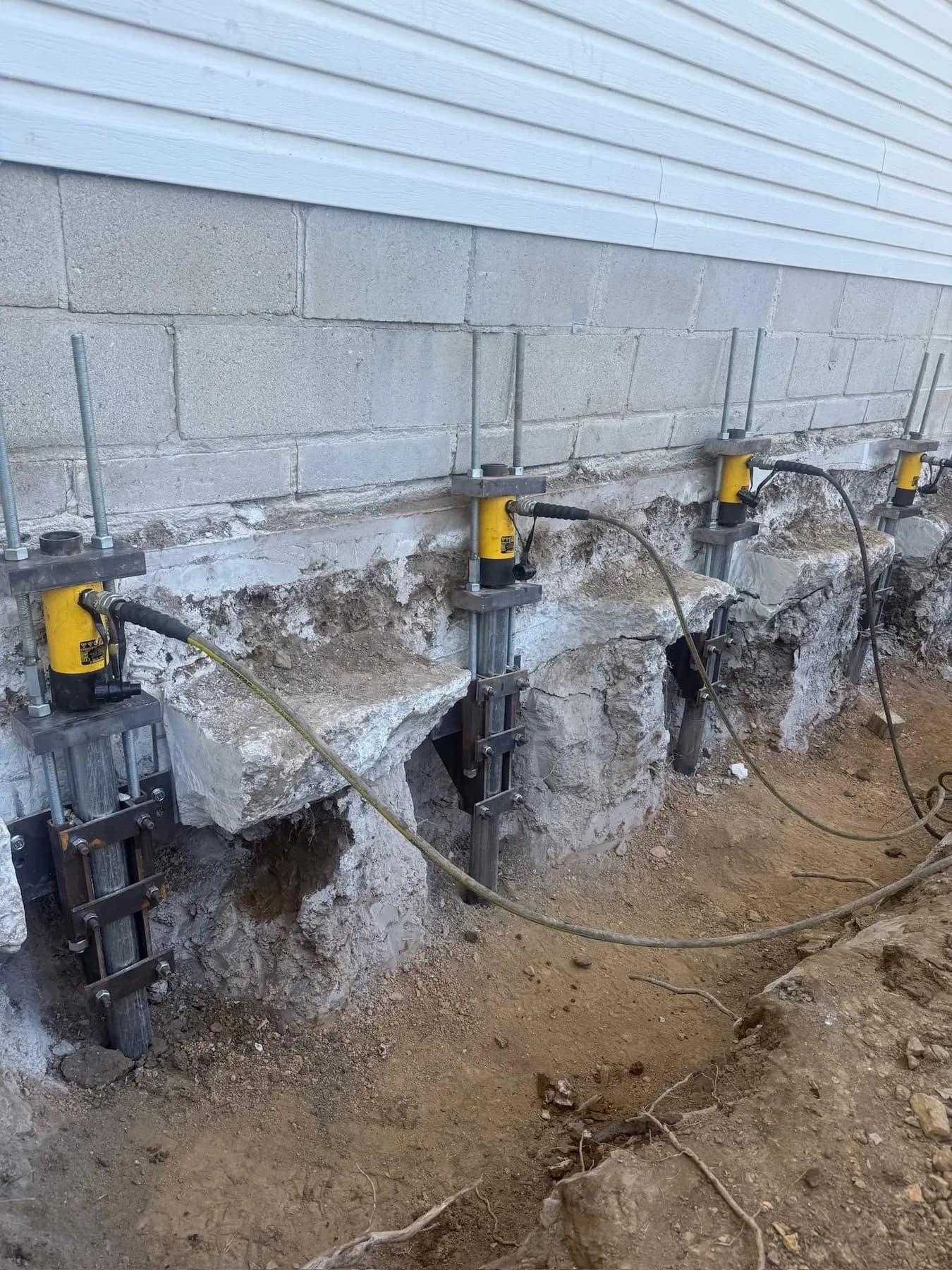 Foundation piers and hydraulic jacks lifting a settled block foundation wall