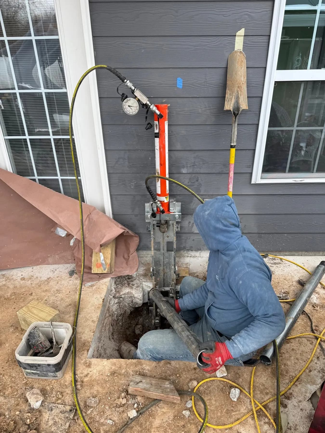 Technician installing a foundation pier beside a home